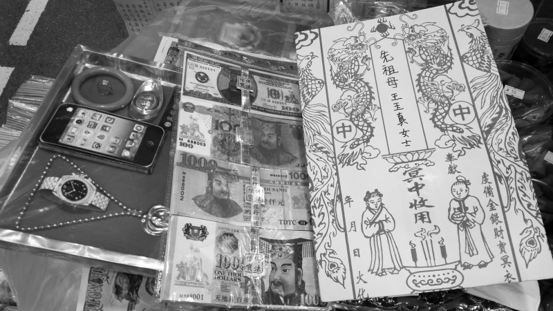 Coffret de l’ensemble : la montre Cartier, le collier, l’IPhone, le bracelet et le lingot d’or pour femme ; les billets de la banque des Enfers ; et l’enveloppe décorée des figures anciennes dans laquelle l’on met les offrandes à brûler. Hong Kong, 2016. 